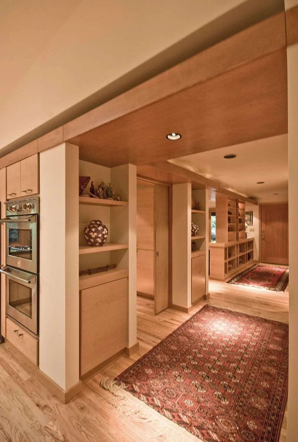 Blonde wood custom cabinetry with built-in shelving and double oven